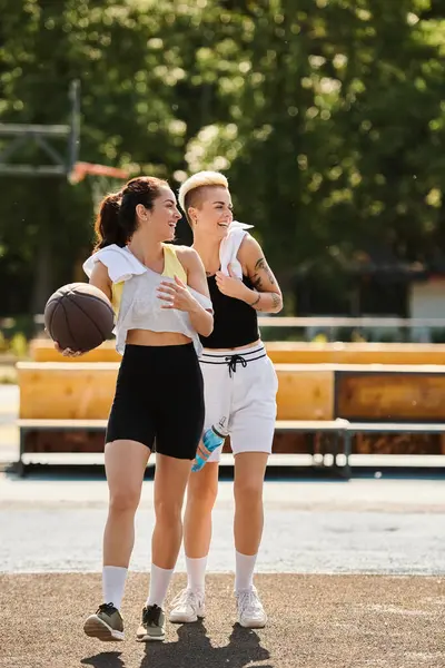 Two athletic young women compete in a spirited game of basketball on an outdoor court in the summer. — Stock Photo