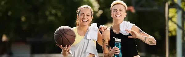 Two young women, friends and athletes, stand side by side outdoors holding a basketball, ready to play a game on a sunny summer day. — Stock Photo
