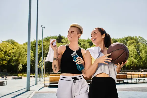 Dos amigas atléticas de pie juntas, sosteniendo pelotas de baloncesto en un entorno al aire libre de verano. — Stock Photo
