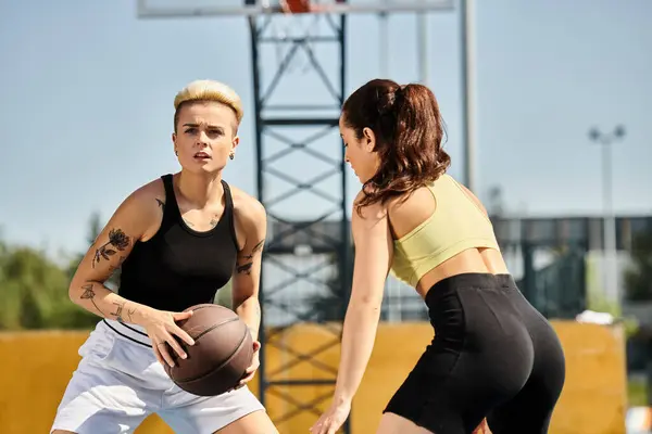 Dos amigas atléticas de pie lado a lado, sosteniendo un baloncesto al aire libre en verano. - foto de stock