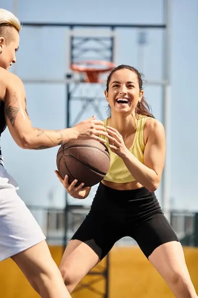 Deux jeunes femmes sportives debout ensemble, dont une tenant un ballon de basket-ball, prêtes à jouer au basket-ball dehors par une journée ensoleillée en été. — Photo de stock