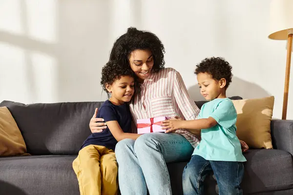 Atractiva mujer afroamericana alegre recibiendo regalo de sus dos lindos hijos, Día de la madre - foto de stock