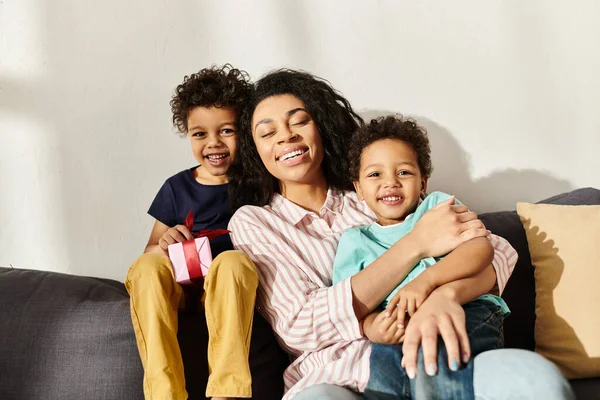 Alegre mujer afroamericana posando con adorables hijos pequeños y mirando a la cámara, Día de las Madres - foto de stock