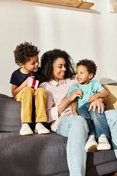 Feliz mujer afroamericana sentada en el sofá con sus lindos hijos y divirtiéndose, Día de la Madre - foto de stock