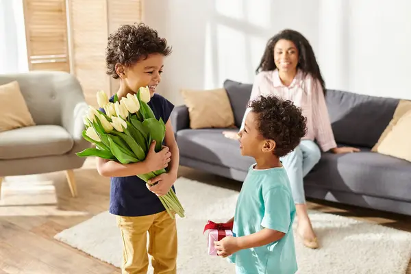 Focus sur les garçons afro-américains tenant des fleurs et des cadeaux à côté de leur mère floue, Fête des mères — Photo de stock