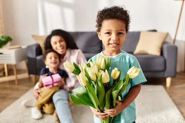 Se concentrer sur joyeux garçon afro-américain tenant des tulipes avec sa mère floue et son frère sur fond — Photo de stock