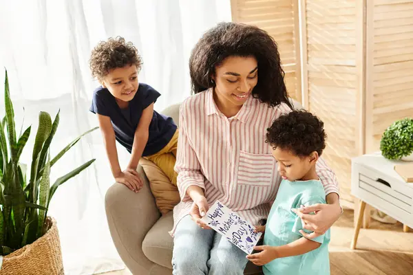 Cheerful african american woman receiving postcard from her two little sons for Mothers day — Stock Photo