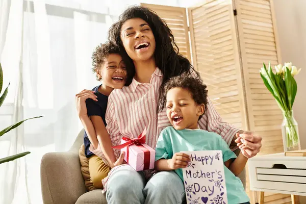 Joyful appealing african american woman receiving postcard and gift from little sons, Mothers day — Stock Photo