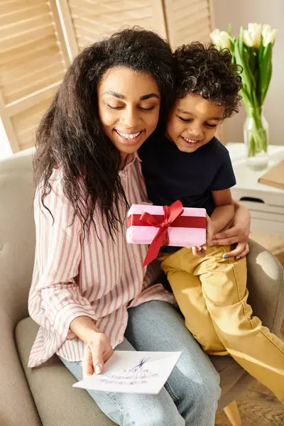 Gioiosa attraente donna africana americana che riceve regalo e cartolina dal suo piccolo figlio, la festa della mamma — Foto stock