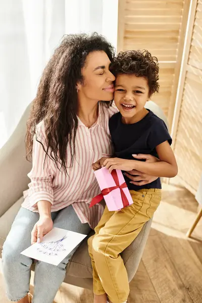 Joliment belle femme afro-américaine recevant cadeau et carte postale de son fils joyeux, fête des mères — Photo de stock