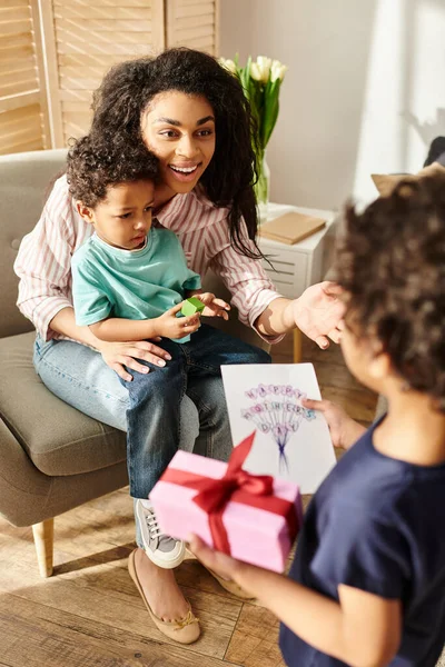 Jolly african american mother holding her cute son and receiving gift and postcard from his brother — Stock Photo