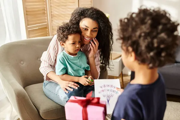 Merry african american mother holding little son and receiving gift and postcard from his brother — Stock Photo