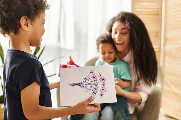 Se concentrer sur le petit garçon afro-américain donnant cadeau et carte postale à sa mère qui tient son frère — Photo de stock