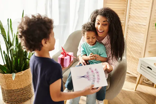 Happy african american woman holding her cute son and receiving gift and postcard from his brother — Stock Photo