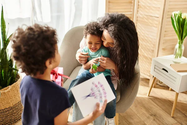Pretty african american woman with her little son receiving postcard and gift from his brother — Stock Photo