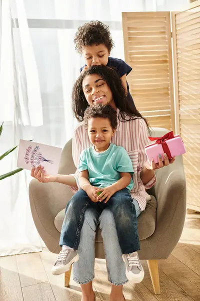 Joyous pretty african american woman spending time with her sons with postcard and gift, Mothers day — Stock Photo