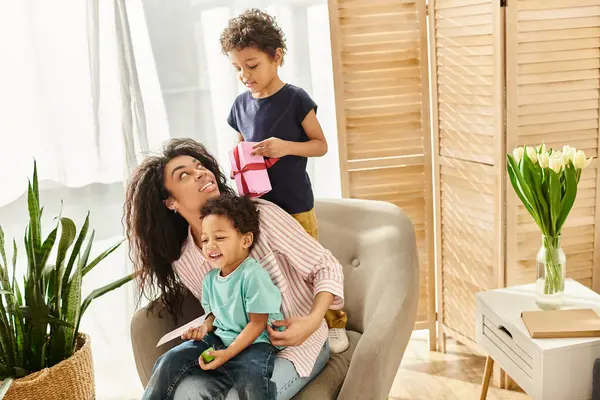 Happy african american woman spending time with her adorable sons, present and postcard, Mothers day — Stock Photo
