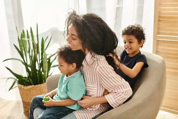 Маленький милий афроамериканський хлопчик плете волосся своєї веселої матері, в той час як вона тримає свого брата — стокове фото