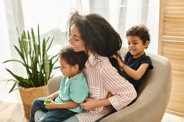 Pequeño lindo africano americano chico trenzando pelo de su alegre madre mientras ella sosteniendo su hermano - foto de stock