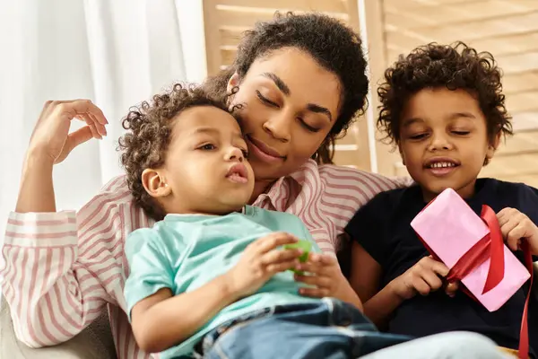 Alegre afroamericana madre pasando tiempo con sus adorables hijos con presente en las manos - foto de stock