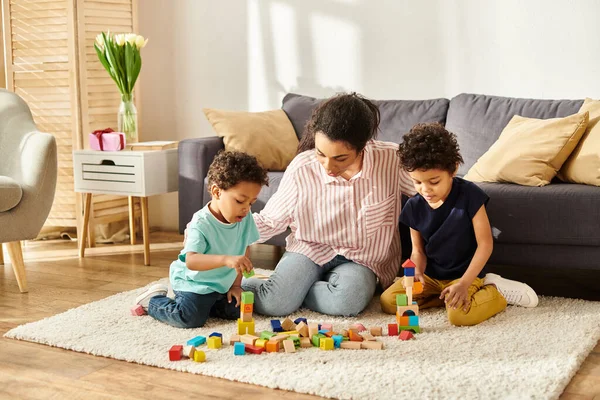 Bien parecido africano americano madre jugando con su lindo niños pequeños con juguetes mientras en casa - foto de stock