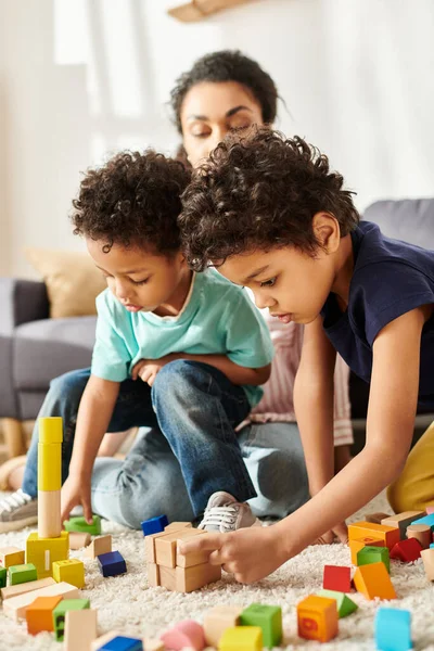 Ansprechende lustige afrikanisch-amerikanische Mutter in kuscheliger Hauskleidung, die Zeit mit ihren verspielten Söhnen verbringt — Stockfoto