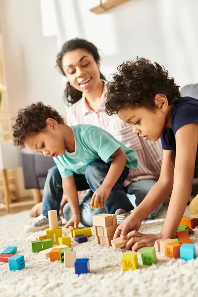 Bien parecido feliz afroamericano madre en acogedora ropa de casa jugando con juguetes con sus adorables hijos - foto de stock