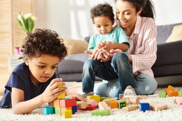 Foco en adorable afroamericano chico jugando con su borrosa madre y hermano en el telón de fondo - foto de stock