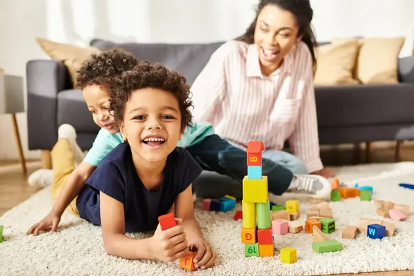 Focus on jolly african american boy smiling at camera with his blurred mom and brother on backdrop — Stock Photo
