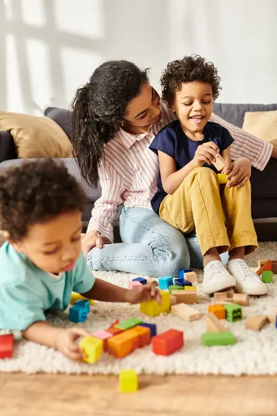 Se centran en la alegre madre afroamericana y su hijo junto a su otro hijo borroso jugando con juguetes - foto de stock