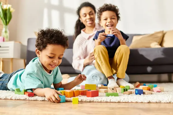 Foco en alegre afroamericano chico jugando con su alegre borrosa madre y hermano en telón de fondo - foto de stock