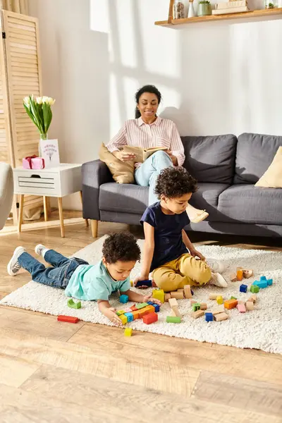 Cheerful african american mother reading book and looking at her playful adorable children — Stock Photo