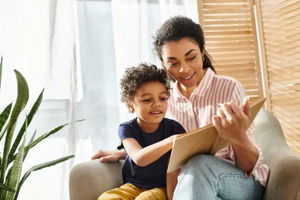 Jolly attractive african american woman in homewear reading book to her adorable son at home — Stock Photo
