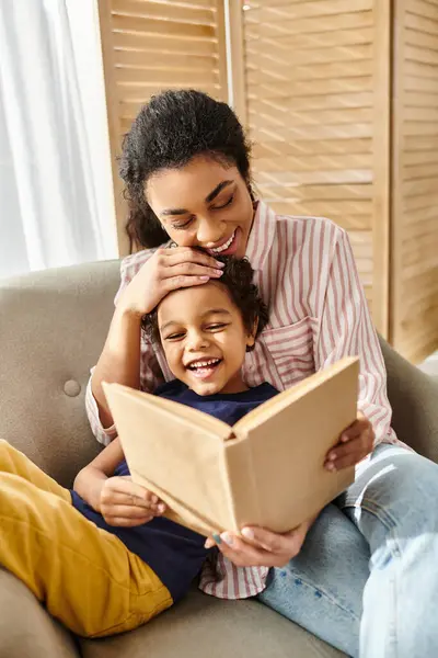 Alegre afroamericana madre y su adorable hijito leyendo libro juntos en casa - foto de stock