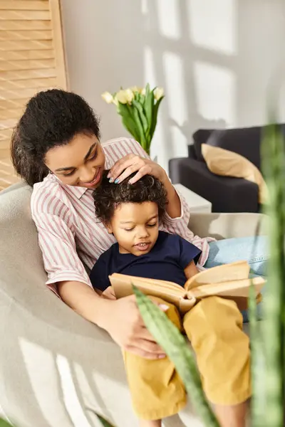 Gioiosa donna afro-americana nel libro di lettura della biancheria da casa con il suo allegro figlioletto a casa — Foto stock