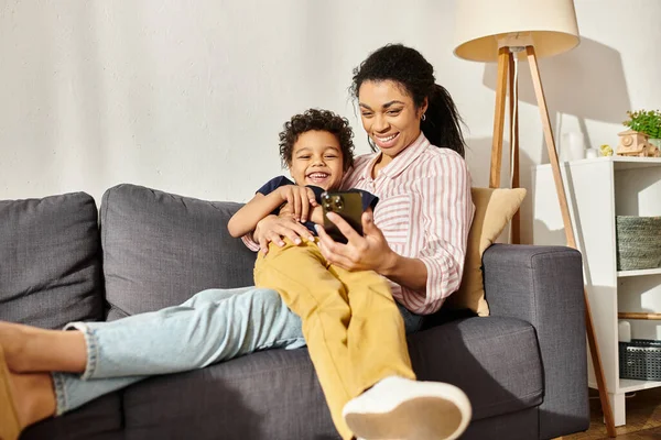 Joyeuse mère afro-américaine étreignant son petit fils et regardant smartphone avec lui — Photo de stock