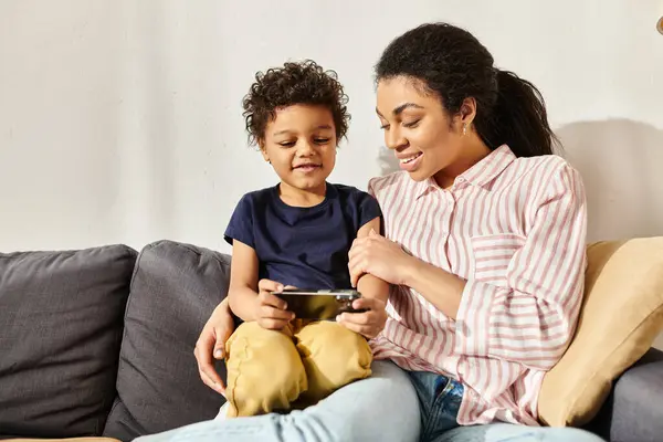 Весела афроамериканська мати та її маленький син дивляться на смартфон, проводячи час разом — стокове фото
