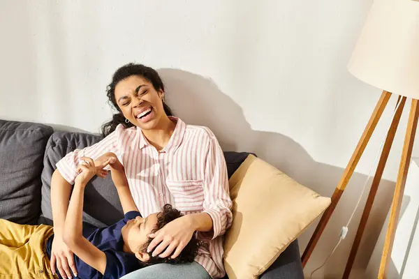 Joyous beautiful african american woman spending time together with her little cute son on sofa — Stock Photo