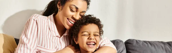 Joyous beautiful african american woman hugging her jolly little son while in living room, banner — Stock Photo