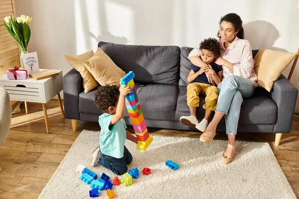 Little cute boy showing tower of cubes to his jolly shocked brother and mother while at home — Stock Photo