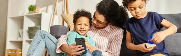 Fröhliche afrikanisch-amerikanische Mutter mit Telefon in der Hand, die Zeit mit ihren beiden entzückenden Söhnen verbringt, Banner — Stockfoto