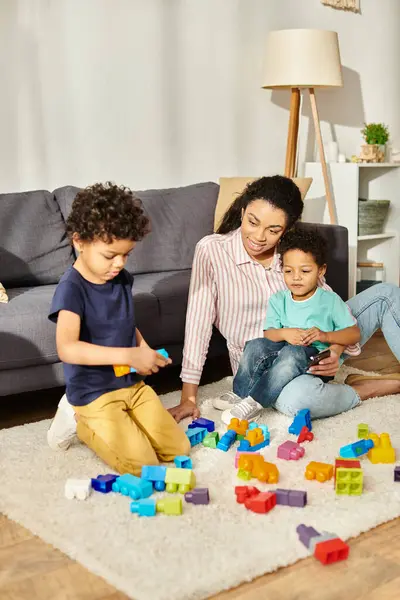 Alegre bela mãe afro-americana assistindo seus adoráveis filhinhos brincando com brinquedos em casa — Fotografia de Stock