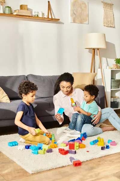Glückliche afrikanisch-amerikanische Mutter in Hauskleidung, die mit ihren entzückenden kleinen Kindern im Wohnzimmer spielt — Stockfoto