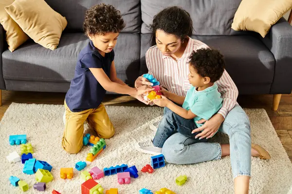 Bela afro-americana mãe em trajes acolhedores brincando com seus filhinhos bonitos na sala de estar — Fotografia de Stock