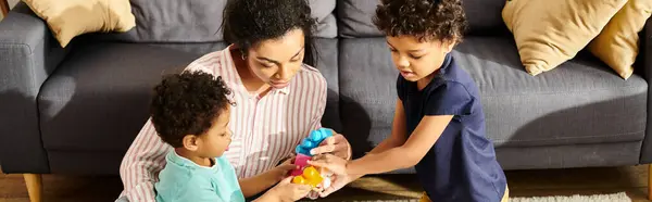 Bien parecido afroamericano madre jugando con sus lindos hijos pequeños en sala de estar, pancarta - foto de stock