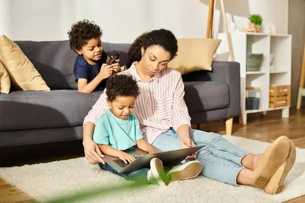 Attraktive afrikanisch-amerikanische Mutter in gemütlicher Homewear, die mit ihren süßen Kindern auf dem Laptop Filme guckt — Stockfoto