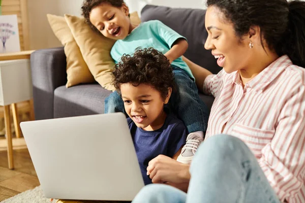 Весёлая привлекательная африканская американская мать смотрит интересные фильмы с двумя маленькими сыновьями — стоковое фото