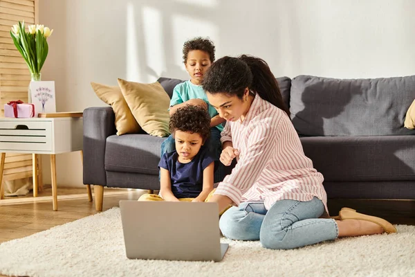 Concentrated african american mother and son looking at laptop with other adorable boy on backdrop — Stock Photo
