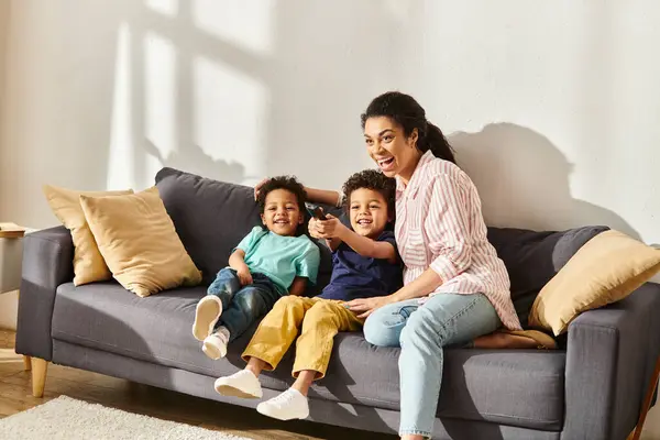 Радостная красивая африканская американка в домашней одежде смотрит фильмы со своими маленькими симпатичными сыновьями — стоковое фото