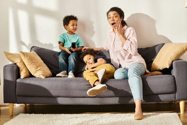 Sorprendida hermosa afroamericana mujer en ropa de casa viendo películas con sus hijos adorables - foto de stock